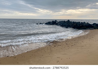 Waves Breaking on Sandy Beach With Coastal Rock Breakwater Under Cloudy Sky