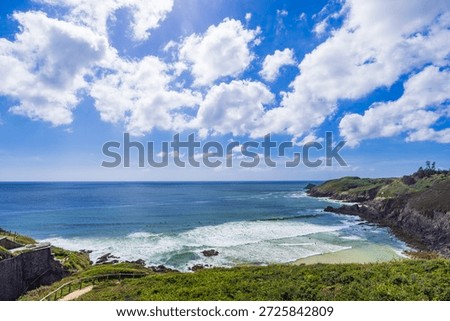 Waves breaking on sandy beach with green cliffs and bright blue sky, Plouzane, Brittany