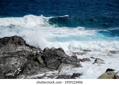 Waves Collide Against A Black Rock Formation.