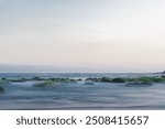 Waves crash against rocks covered in moss and seaweed on the shore. The image was taken using a slow shutter speed with a silky water effect. beautiful nature concept.