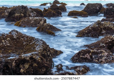 Waves crash against rocks covered in moss and seaweed on the shore. The image was taken using a slow shutter speed with a silky water effect. beautiful nature concept. - Powered by Shutterstock