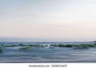 Waves crash against rocks covered in moss and seaweed on the shore. The image was taken using a slow shutter speed with a silky water effect. beautiful nature concept. - Powered by Shutterstock