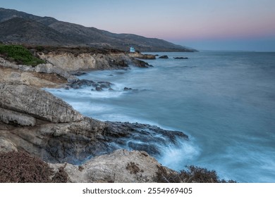 Waves crash against rocky cliffs at Leo Carrillo State Beach during twilight, overlooking the tranquil ocean and distant mountains in Malibu. - Powered by Shutterstock