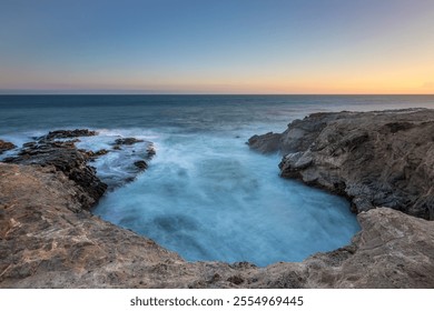 Waves crash against rocky formations as the sun sets over Leo Carrillo State Beach, casting a serene glow on the ocean. - Powered by Shutterstock