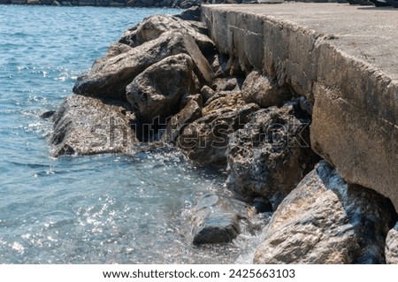 Waves crash against a stone pier with a walkway.