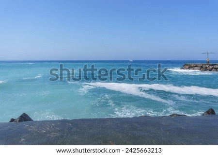 Waves crash against a stone pier with a walkway. 
