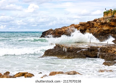 Waves Crash On Rocks. Solid As A Rock. Cloudy Blue Sky. Rough Water