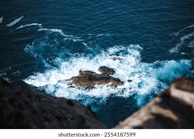 Waves crashing against isolated rocky formations in the deep blue ocean, viewed from high cliff edge .  - Powered by Shutterstock