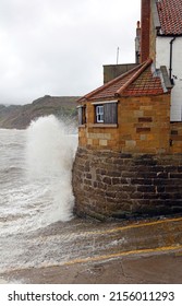 Waves crashing against the old Coastguard Station, Robin Hoods Bay Yorkshire England
					
