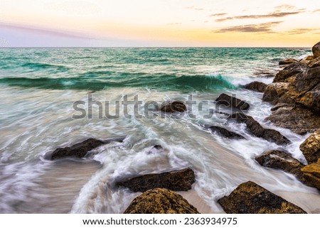 Waves crashing gently on the shore in Destin by East Jetty with a warm, vibrant sunset