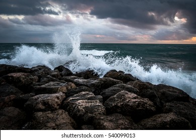 Waves crashing on the black rocks beneath a dark sky