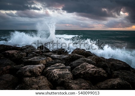 Waves crashing on the black rocks beneath a dark sky