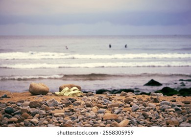 Waves crashing on a rocky shore with surfboard straps resting on pebbles at sunset - Powered by Shutterstock