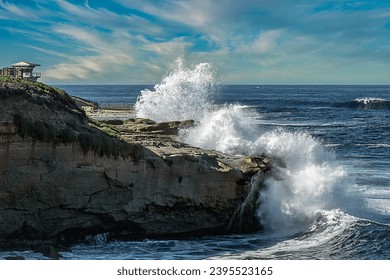 WAVES CRASHING ON THE ROCKY SHORELINE IN LA JOLLA CALIFORNIA NEAR THE LIFEGUARD STATION AND THE CHILDRENS POOL WITH A NICE LIGHTLY CLOUDY SKY