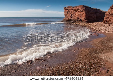 Waves crashing on stone shore below red PEI cliffs at North Cape