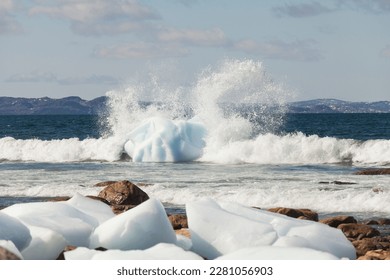Waves crashing onto an iceberg close to the shoreline in Newfoundland and Labrador, Canada.