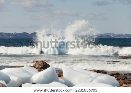 Waves crashing onto an iceberg close to the shoreline in Newfoundland and Labrador, Canada.