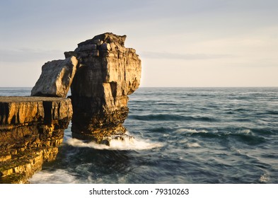 Waves Crashing Over Rock Formation Cliffs At Sunset With Beautiful Light On Rock Faces