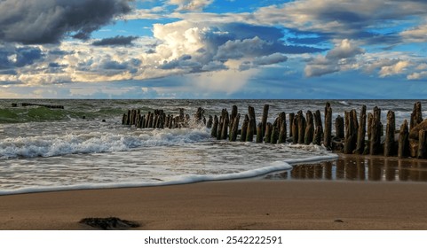 Waves gently lapping against wooden posts on a serene sandy beach under a vibrant sky near the coastline - Powered by Shutterstock