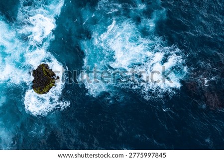 Waves hitting volcanic rocks and shallow reef, aerial top down view
