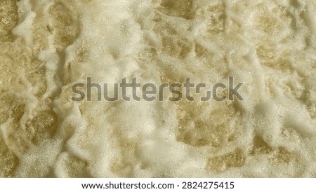 Waves move towards the beach, bubbling and creating foam as they hit the sand. The water appears rough and lively under the sun's light. A typical beach scene unfolds.