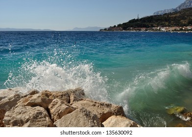 Waves on beautiful beach with stones in Podgora, Croatia. In background with mountain Biokovo and monument Seagull's wings