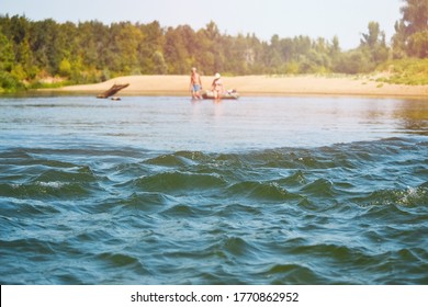 Waves On The River Roll, Unrecognizable Travelers Are Walking On The Water In The Distance And Pulling An Inflatable Boat. Electoral Focus