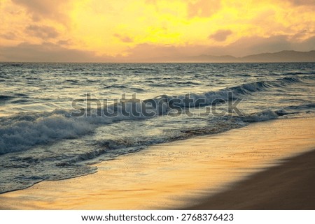 Waves on a sandy ocean beach under a beautiful sunset sky with clouds in Santa Monica. LA. USA.