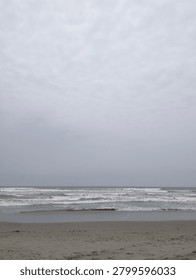 Waves rolling onto a sandy beach under a cloudy sky, creating a calm and natural coastal seascape with a peaceful atmosphere.