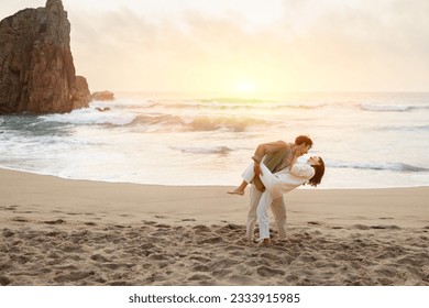 Waves of romance. Young romantic couple dancing on beach at sunset, enjoying date near ocean shore, free space, full length. Loving guy and lady walking on coastline - Powered by Shutterstock