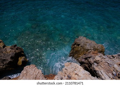 Waves Splash Against Rocks. Marine Theme With Copy Space. Top View Natural Background Of Rippled Sea-green Sea Water. Aerial View Of Aquamarine Sea Surface. Rough Sea And Stone Texture.