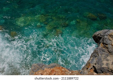 Waves Splash Against Rocks. Marine Theme With Copy Space. Top View Natural Background Of Rippled Sea-green Sea Water. Aerial View Of Aquamarine Sea Surface. Rough Sea And Stone Texture.