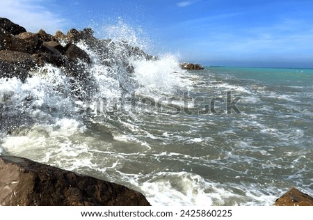 Waves splash on stones in sea. Breakwater with sea waves. Wave at stone pier. Wave in a storm breaks on stones at pier. Waves splash on stones at coast beach. Sea waves breaking on rocks in ocean.