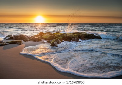 Waves splash over boulders as foaming  water soaks the beach at sunrise in Beach Haven, NJ