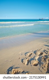Waves washing onto sandy beach shore with footprints on a tropical and exotic resort with clear blue sky background and copyspace. Relaxing summer seascape to enjoy a peaceful holiday - Shutterstock ID 2175130991