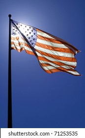 Waving American Flag, Clear Blue Sky, Sun Is Directly Behind The Flag