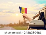 Waving the Andorra flag against the sunrise or sunset from a car driving along a country road. Holding the Andorra flag, traveling by car, on a weekend trip.