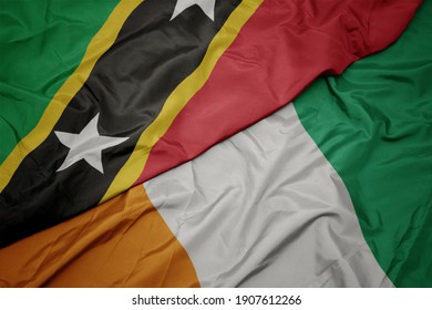 waving colorful flag of cote divoire and national flag of saint kitts and nevis. macro
