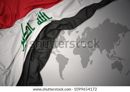 waving colorful national flag of iraq on a gray world map background.