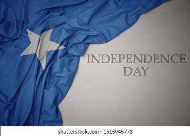 waving colorful national flag of somalia on a gray background with text independence day. concept