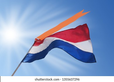 Waving Dutch Flag With Orange Streamer On Blue, Sunny Sky. Koningsdag (Kingsday) And Bevrijdingsdag (Liberation Day) In The Netherlands.