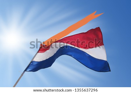 Waving dutch flag with orange streamer on blue, sunny sky. Koningsdag (Kingsday) and Bevrijdingsdag (Liberation Day) in the Netherlands.