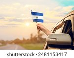Waving the El Salvador flag against the sunrise or sunset from a car driving along a country road. Holding the El Salvador flag, traveling by car, on a weekend trip.