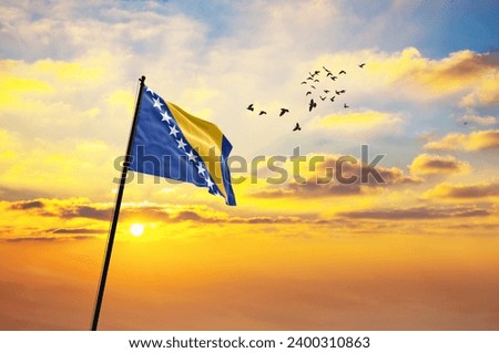Waving flag of Bosnia and Herzegovina against the background of a sunset or sunrise. Bosnia and Herzegovina flag for Independence Day.