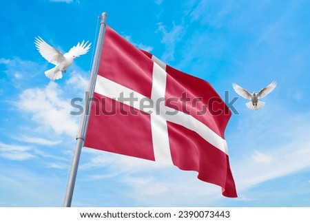 Waving flag of Denmark in beautiful sky and flying pigeons. Denmark flag for independence day. The symbol of the state on wavy fabric.