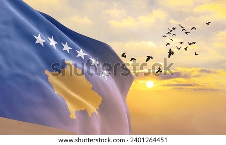 Waving flag of Kosovo against the background of a sunset or sunrise. Kosovo flag for Independence Day. The symbol of the state on wavy fabric.