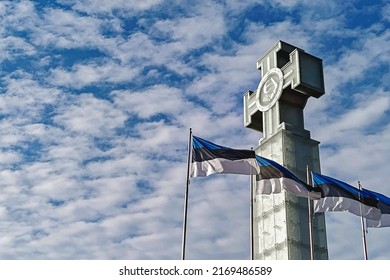 Waving flags of Estonia on blue sky and monument to fallen in War of Independence in Tallinn Freedom square. Estonian independence day is celebrated on February 24