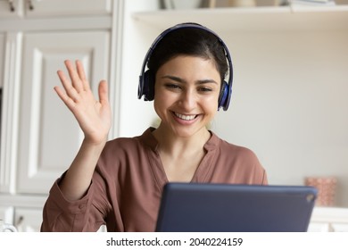 Waving Hand. Friendly Indian Female In Earphones Foreign Language Teacher Give Online Class By Pad Webcam Welcome Student On Lesson. Positive Young Biracial Lady Mentor Coach Greet Audience On Webinar