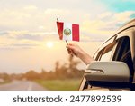 Waving the Peru flag against the sunrise or sunset from a car driving along a country road. Holding the Peru flag, traveling by car, on a weekend trip.