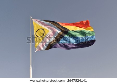 Waving intersex‑inclusive Progress Pride flag on blue sky—celebrating visibility and inclusion within LGBTQIA+.
